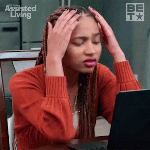 A Woman Is Sitting At A Table With Her Hands On Her Head While Looking At A Laptop Computer . GIF