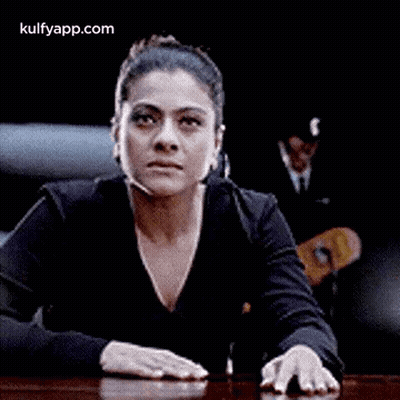 A Woman Is Sitting At A Table With Her Hands On The Table And Making A Funny Face . GIF