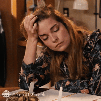 A Woman Is Sitting At A Table With Her Head Resting On Her Hand And The Word Schitts Creek Is On The Bottom Right GIF