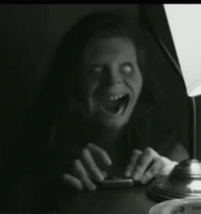 A Woman Is Sitting At A Table With Her Mouth Open And A Lamp In The Background . GIF