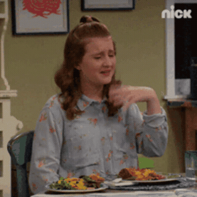 A Woman Is Sitting At A Table With Plates Of Food And A Nick Logo Behind Her GIF