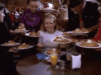 A Woman Is Sitting At A Table With Plates Of Pancakes And A Glass Of Orange Juice . GIF