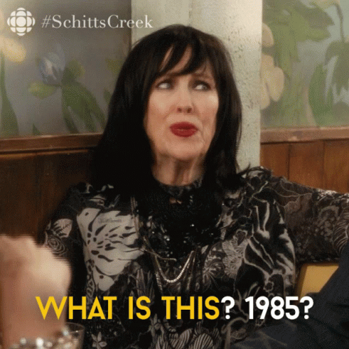 mujer sentada en una mesa con las palabras qué es esto 1985 abajo GIF
