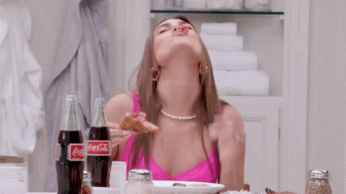 A Woman Is Sitting At A Table With Two Bottles Of Coca Cola GIF