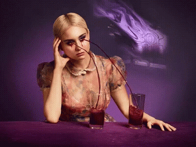A Woman Is Sitting At A Table With Two Glasses Of Red Liquid Being Poured Into Her GIF