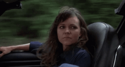 A Woman Is Sitting In A Car And Looking Out The Window . GIF