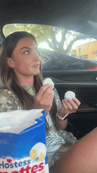 A Woman Is Sitting In A Car Holding A Bag Of Hostess Softies GIF
