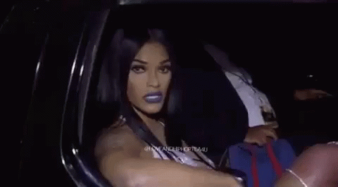 A Woman Is Sitting In A Car Making A Funny Face And Pointing At The Camera . GIF