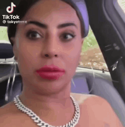 A Woman Is Sitting In A Car Wearing A Necklace And Red Lipstick . GIF