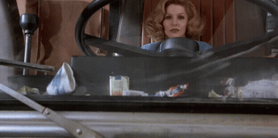 A Woman Is Sitting In A Car With A Steering Wheel GIF