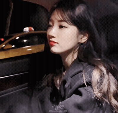 A Woman Is Sitting In A Car With A Taxi Cab In The Background GIF