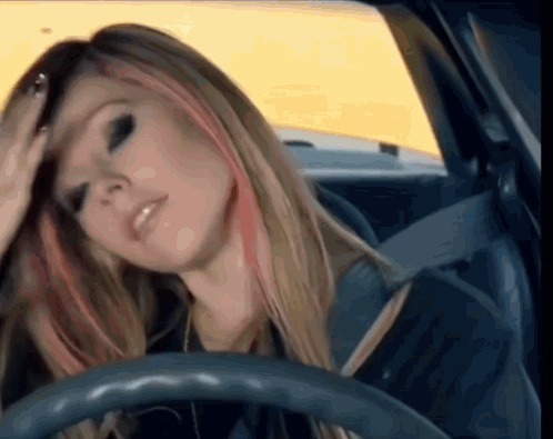 A Woman Is Sitting In A Car With Her Hand On Her Head . GIF