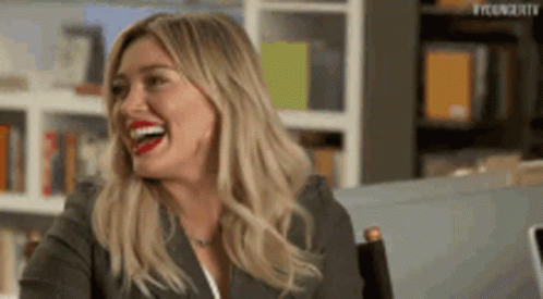 A Woman Is Sitting In A Chair And Laughing With Her Mouth Open . GIF
