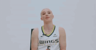 A Woman Is Sitting In A Chair And Smiling While Wearing A Basketball Uniform . GIF
