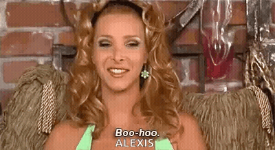 A Woman Is Sitting In A Chair And Smiling While Wearing A Green Top And Earrings . GIF