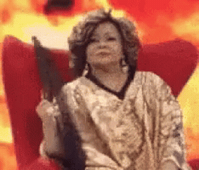 A Woman Is Sitting In A Chair Holding A Fan In Front Of Flames . GIF