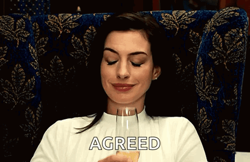 A Woman Is Sitting In A Chair Holding A Glass Of Champagne And The Word Agreed Is On The Bottom Of Her Shirt GIF