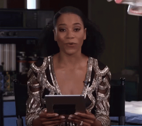 A Woman Is Sitting In A Chair Holding A Tablet In Her Hands GIF