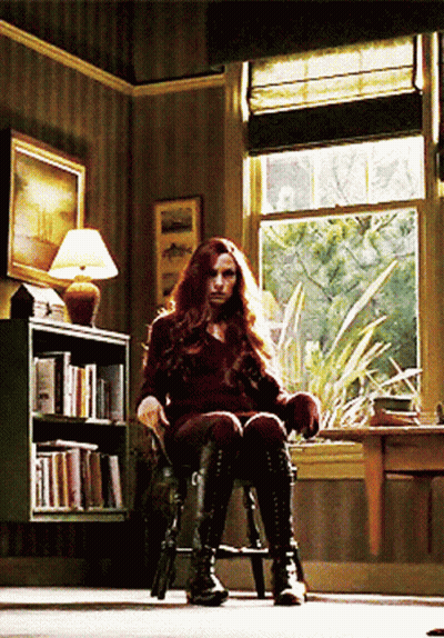 A Woman Is Sitting In A Chair In Front Of A Bookshelf GIF