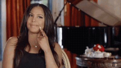 A Woman Is Sitting In A Chair In Front Of A Piano And Pointing To Her Face . GIF
