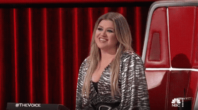 A Woman Is Sitting In A Chair In Front Of A Red Curtain On A Stage . GIF