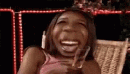 A Woman Is Sitting In A Chair Laughing And Holding A Glass Of Wine . GIF