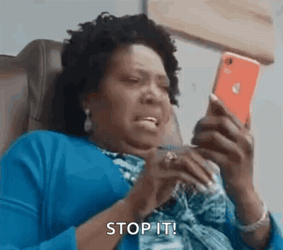 A Woman Is Sitting In A Chair Looking At Her Cell Phone And Making A Funny Face . GIF