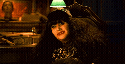 A Woman Is Sitting In A Chair Making A Devil Horns Sign With Her Hand . GIF
