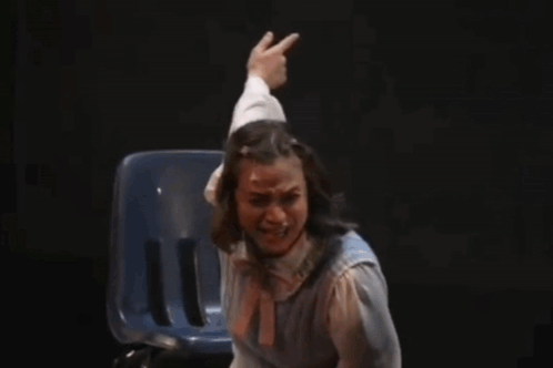 A Woman Is Sitting In A Chair On A Stage While A Man Reaches Out To Her . GIF