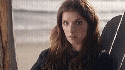 A Woman Is Sitting In A Chair On The Beach With A Surfboard . GIF