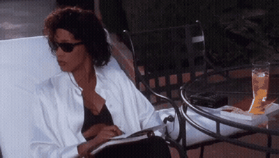 A Woman Is Sitting In A Chair Reading A Book Next To A Table . GIF