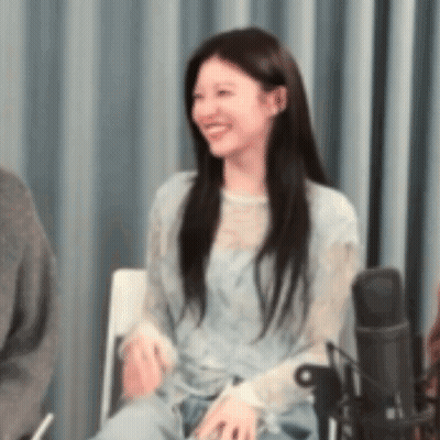 A Woman Is Sitting In A Chair Smiling In Front Of A Microphone In A Room . GIF