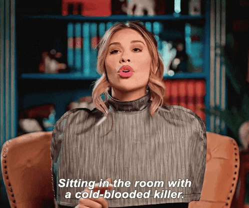 A Woman Is Sitting In A Chair With A Sign That Says Sitting In The Room With A Cold-Blooded Killer GIF