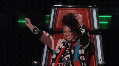 A Woman Is Sitting In A Chair With Her Arms In The Air And Smiling . GIF