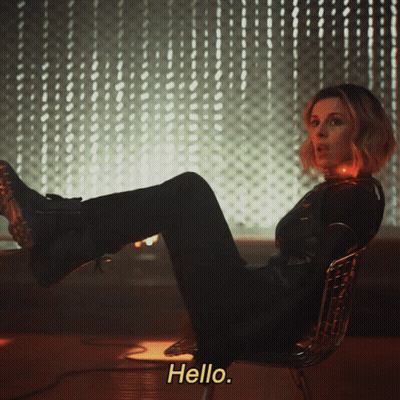A Woman Is Sitting In A Chair With Her Feet Up And The Words Hello Behind Her GIF