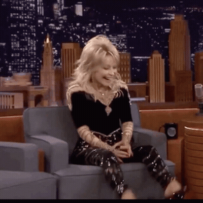 A Woman Is Sitting In A Chair With Her Legs Crossed And Laughing GIF