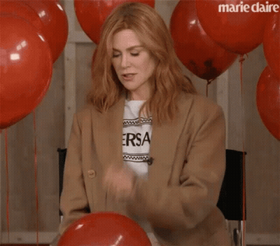 A Woman Is Sitting In A Chair With Red Balloons And Confetti Falling On Her . GIF