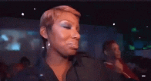 A Woman Is Sitting In A Crowd Of People In A Dark Room And Making A Funny Face . GIF