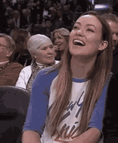 A Woman Is Sitting In A Crowd Of People Laughing . GIF