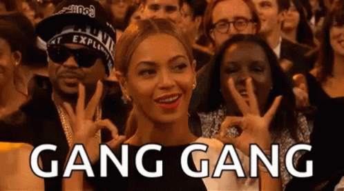 A Woman Is Sitting In A Crowd Of People Making A Peace Sign And The Word Gang Gang Is Written Above Her . GIF