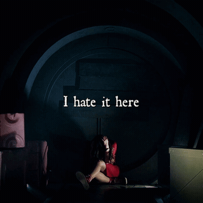A Woman Is Sitting In A Dark Room With The Words I Hate It Here Written Above Her GIF