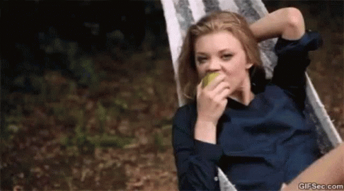 A Woman Is Sitting In A Hammock And Eating An Apple . GIF