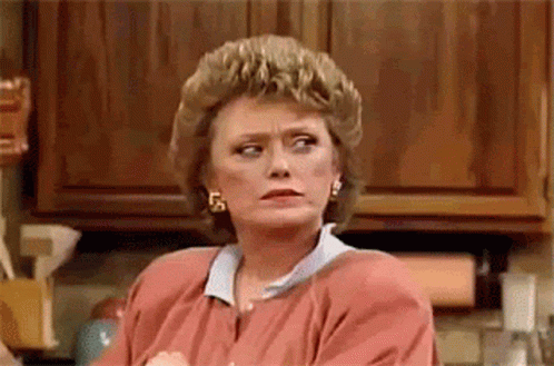 A Woman Is Sitting In A Kitchen With Her Arms Crossed And Looking At The Camera . GIF