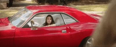 A Woman Is Sitting In A Red Car With Her Head Out The Window . GIF