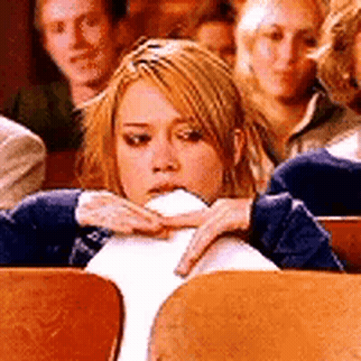 A Woman Is Sitting In A Row Of Wooden Chairs With Her Hand On Her Face . GIF