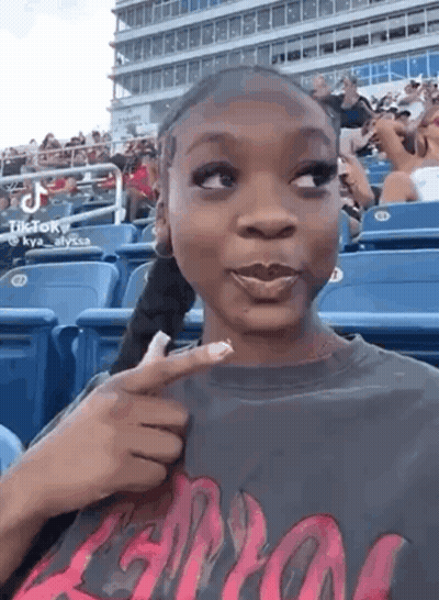A Woman Is Sitting In A Stadium Holding A Piece Of Paper In Her Hand . GIF