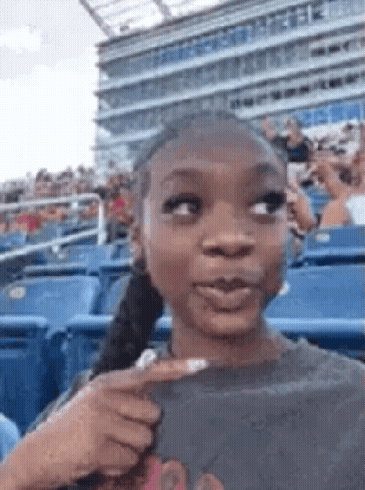 A Woman Is Sitting In A Stadium With A Ponytail And Pointing At Something . GIF