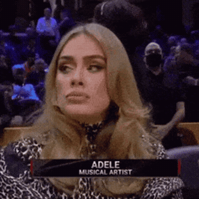 A Woman Is Sitting In A Stadium With A Sign That Says Adele Musical Artist On It . GIF