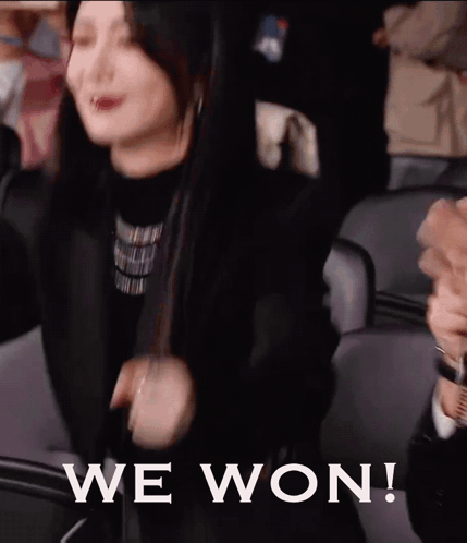 A Woman Is Sitting In A Stadium With Her Arms In The Air And The Words We Won Written On The Bottom . GIF