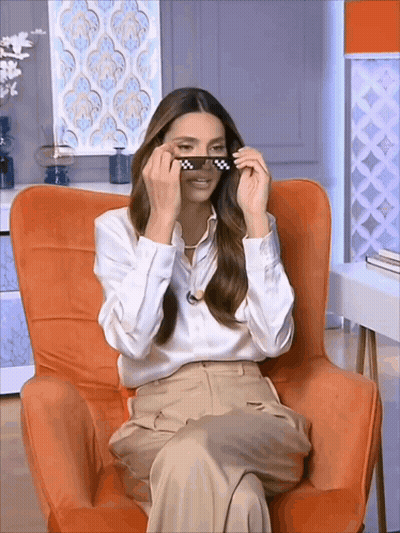 A Woman Is Sitting In An Orange Chair And Wearing Sunglasses GIF